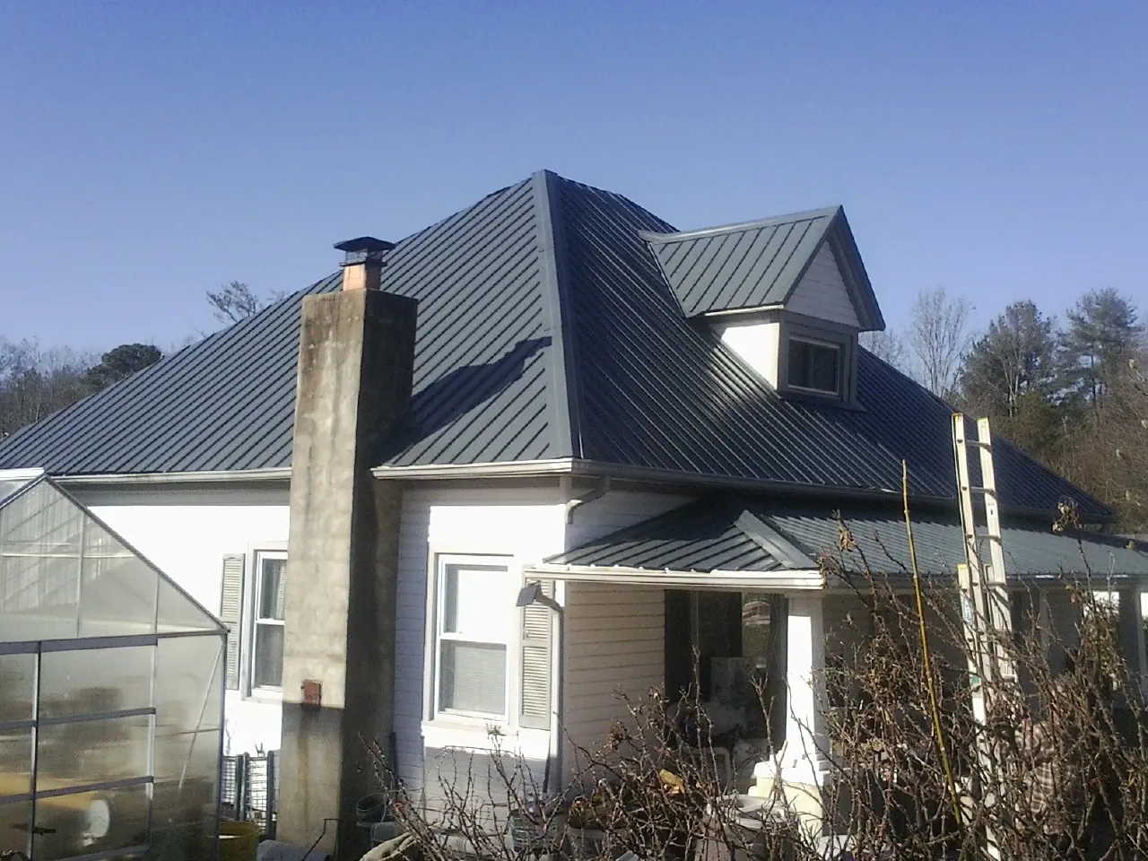 Dark blue standing seam metal roof on a white farmhouse with dormer — Slate & Tile Roof Repair by Roofing Brothers in Platte Center