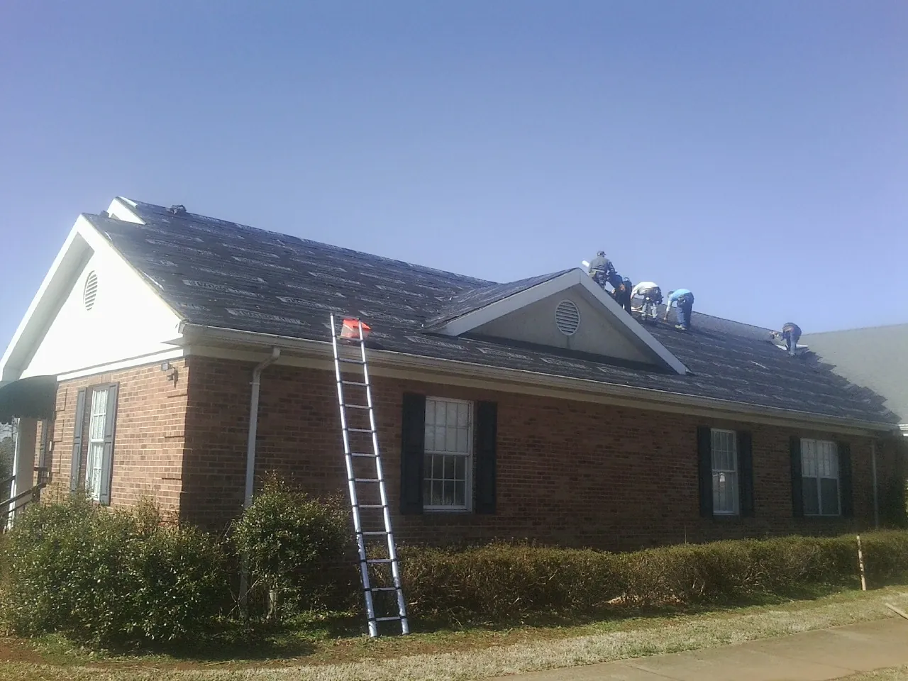 Crew tearing shingles off a brick ranch roof with a ladder set — Emergency Roof Repair work by our crew in Platte Center