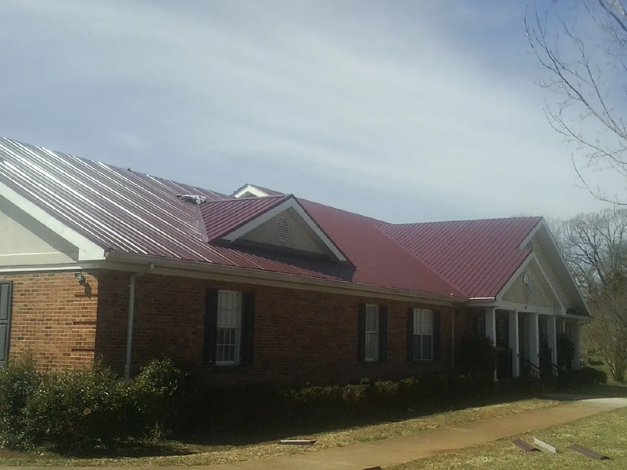 Red metal roof with gabled entries on a long brick building, from a Hail Damage Roof Repair job in Platte Center