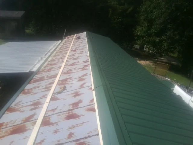 Old rusted panels beside newly installed green metal roofing in Platte Center