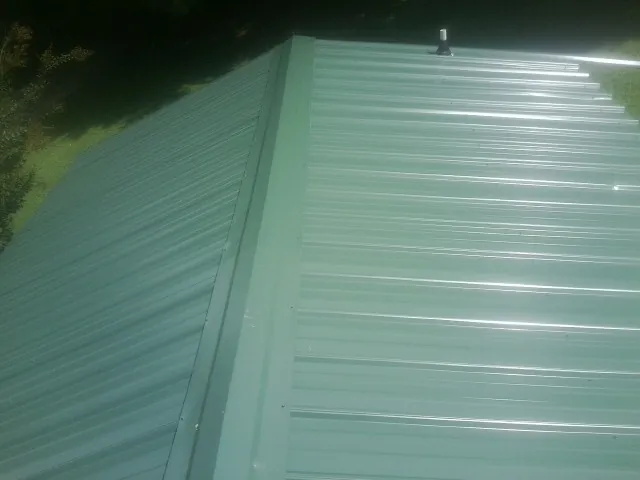 New green metal panels meeting at the ridge of a roof — Flat Roof Repair work by our crew in Platte Center