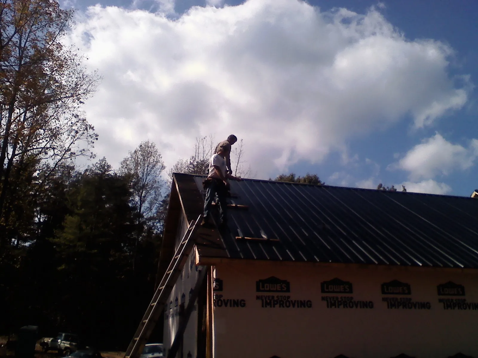 Roofer fastening dark metal panels high against a cloudy sky, from a Roof Inspection job in Platte Center