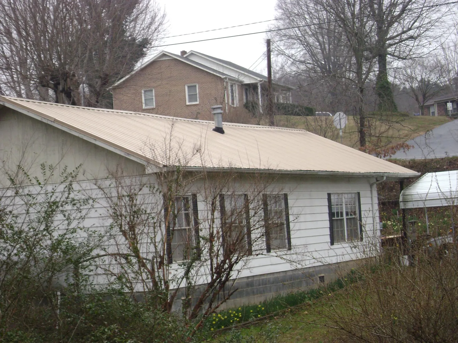 Tan metal roof on a white sided house set into a hillside — Commercial Roofing by Roofing Brothers in Platte Center