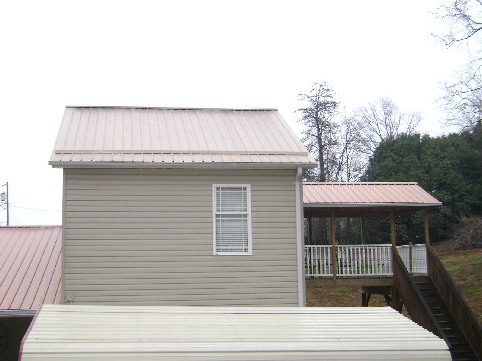 Tan metal roofs on a two story addition and attached porch, from a Roof Replacement job in Platte Center
